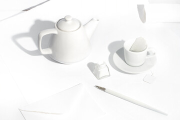 White minimalist scene with a teapot, classic cup, writing pen, ink and envelope