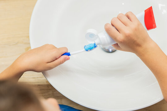 Anonymous child putting toothpaste on toothbrush