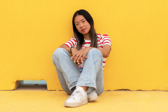 Asian woman sitting on floor against yellow background