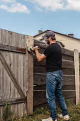 A man with a powerful tool with an angle grinder cleans the wood of the fence - grinding the boards with a coarse grinder brush