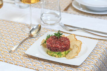 tuna tartar on a bed of chopped avocado and bread chips served with a knife and fork with a glass of water and wine