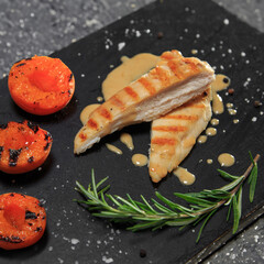 grilled chicken breast with apricot garnish on a black ceramic board