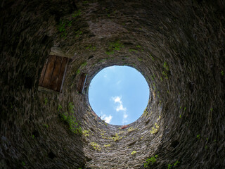 Stone well hole, old construction from inside, brick walls and blue sky background, fall down in the well concept