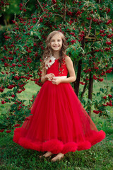 Obraz na płótnie Canvas Little cheerful girl in long red dress standing near tree with red berries and laughing in green summer park, vertical outdoor colorful emotional kid's full length portrait, idea of happy childhood 