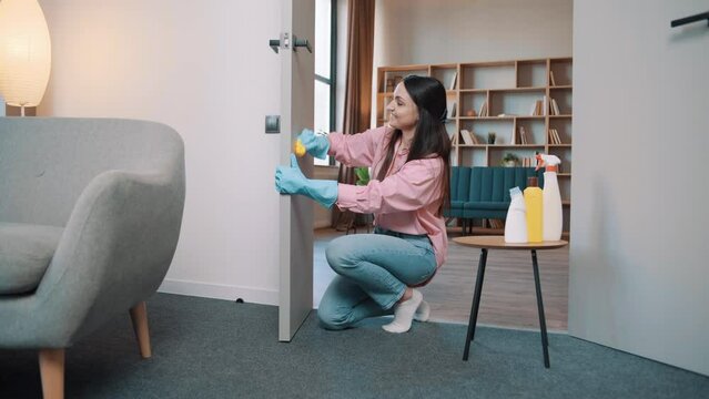 Girl in rubber gloves cleaning door knob. Housewife wash doors in hotel. A Yorkshire Terrier dog runs in the background