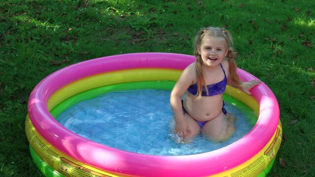 Children in the pool, it's hot in the summer. A little girl. A child plays in a children's pool. Swimming in the yard, inflatable pool in the shade. The girl loves water. Happy child in a swimsuit