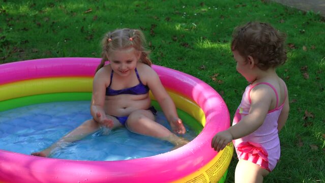 Children in the pool, it's hot in the summer. A little girl. A child plays in a children's pool. Swimming in the yard, inflatable pool in the shade. The girl loves water. Happy child in a swimsuit