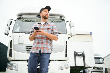 Professional driver using mobile phone while standing in front of his truck. Copy space.