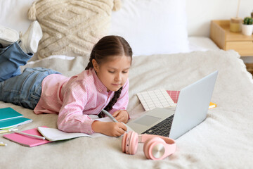 Little girl with laptop studying computer sciences online in bedroom