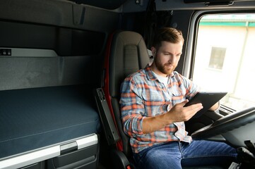 Man truck driver sitting behind wheel of car and holding digital tablet in his hands