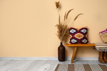 Wooden bench with cushion and pampas grass near beige wall