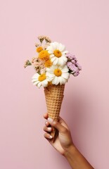 Female hand holding a waffle cone with wildflowers on a pink background