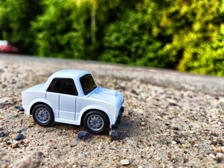 A small white toy car on the background of a natural landscape. The concept of travel and adventure by car. Freedom of movement on your own transport. Blur and partial focus