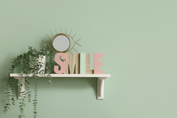 Shelf with small mirror, wooden letters spelling word SMILE and houseplant hanging on green wall