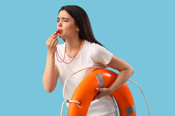 Female lifeguard with ring buoy whistling on blue background