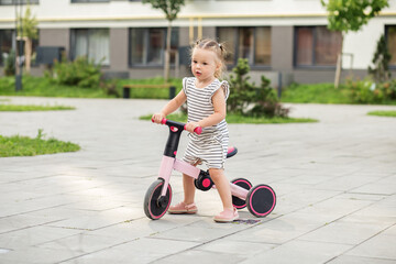 Toddler girl driving balance bike outdoors. Learning to ride bike concept.