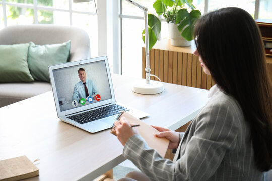 Beautiful woman writing notes during online job interview at home