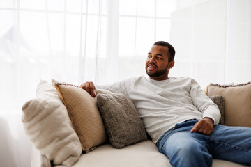 Smiling young african american man relaxing on couch with pillows at home, copy space