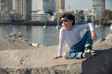 Fototapeta na wymiar Boy in jeans and white pants with sunglasses posing for a photo in fashion editorial on the beach