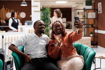 Young couple talking on videocall after arriving at hotel, waiting to check in and sitting in...