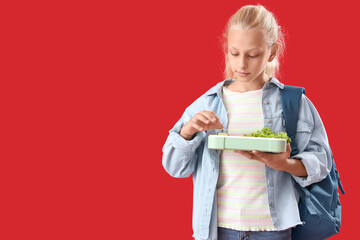 Happy girl with backpack and lunchbox on red background