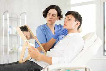 Obraz premium Middle-aged female doctor consulting young man patient lying on medical chair