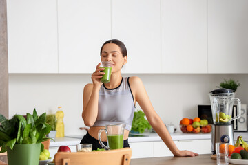 Sporty young woman drinking healthy smoothie in kitchen