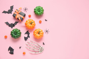 Composition with skeleton hand, gift box, pumpkins, paper bats and spiders on pink background. Halloween celebration concept