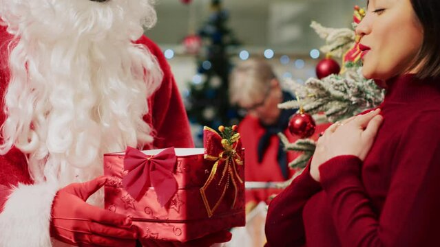 Santa Claus in festive adorn fashion shop holding collecting box acting as Christmas present, receiving raffle ticket from asian client hoping to win big prize during winter holiday season