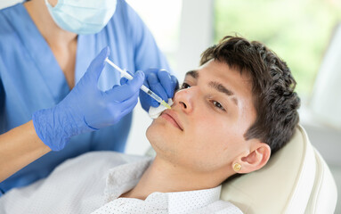 Young male patient lying on clinical chair undergoing face care procedure by injection method