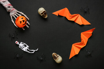 Frame made of skeleton hand, skulls, spiders and paper bats for Halloween celebration on dark background
