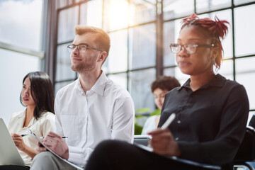 Interested happy young multiracial colleagues sitting on chairs, listening to male boss team leader