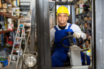 Portrait of confident hispanic worker driving forklift in building materials store