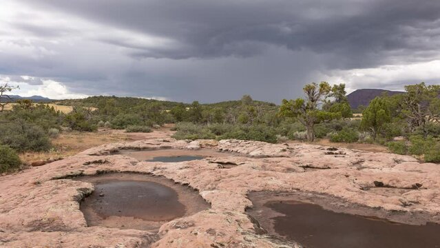 A 4K time lapse video of a summer monsoon storm on the horizon seen from a rocky ridge with some ephemeral pools that are beginning to dry up. A couple of lightning bolts strike the distant mountain.