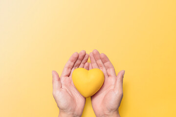hands holding a yellow resin heart against a matching yellow background, symbolizing mental health...