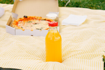 Orange juice mockup in a glass bottle on a background of pizza on a yellow picnic mat. Concept of production of natural multivitamin, peach, fruit juices and their use.