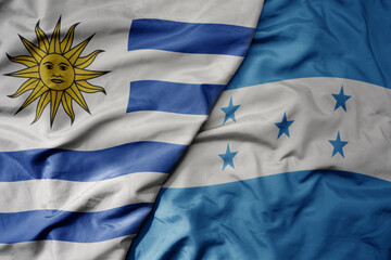 big waving realistic national colorful flag of uruguay and national flag of honduras .