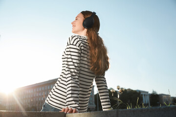 Smiling woman in headphones listening to music outdoors, low angle view