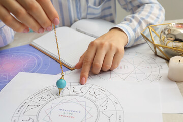 Astrologer using zodiac wheel and pendulum for fate forecast at table, closeup. Fortune telling