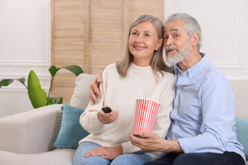 Happy senior couple with popcorn on sofa indoors
