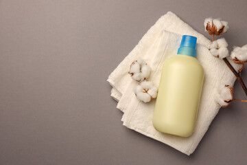 Bottle of fabric softener, terry towel and beautiful cotton flowers on gray background, top view. Space for text