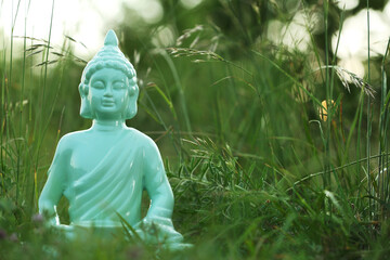 Decorative Buddha statue in green grass outdoors, space for text