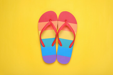 Rainbow flip flops on yellow background, flat lay. LGBT pride