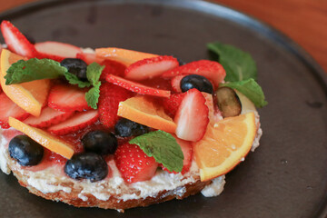 Toast bread with berries, orange and cream on black plate. Traditional sweet breakfast. Healthy fruit sandwiches.