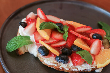Toast bread with berries, orange and cream on black plate. Traditional sweet breakfast. Healthy fruit sandwiches.