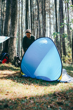 Asian male hiker is setting up a bright blue tent in the forest. Concept of tourism, hiking and staying in nature.