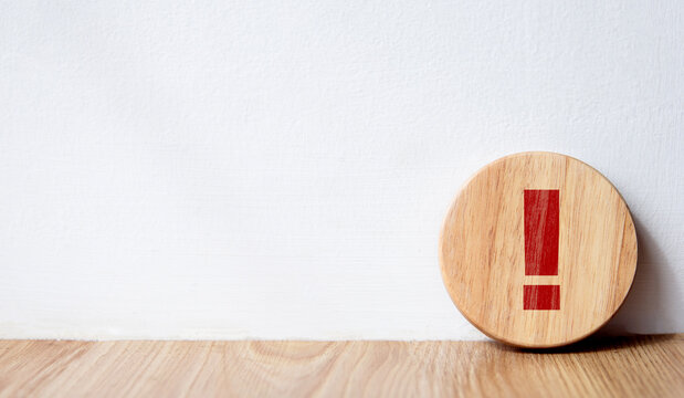 Red exclamation mark on circular wooden block on white background with copy space.