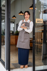 A friendly Asian female coffee shop or restaurant staff standing at the entrance door with a tablet