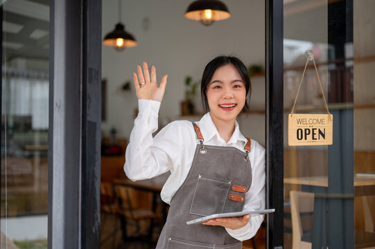 A friendly Asian female coffee shop or restaurant staff standing at the entrance door