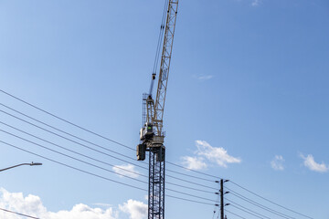 Yellow and black construction crane lifting load near power lines - blue sky with clouds. Taken in...